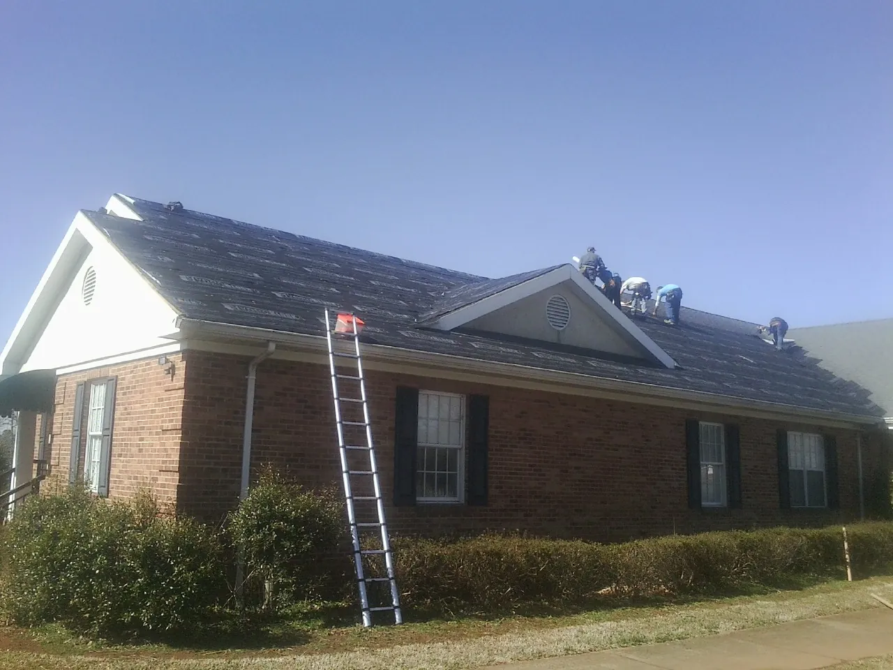 Crew tearing shingles off a brick ranch roof with a ladder set — Metal Roof Repair work by our crew in Humboldt