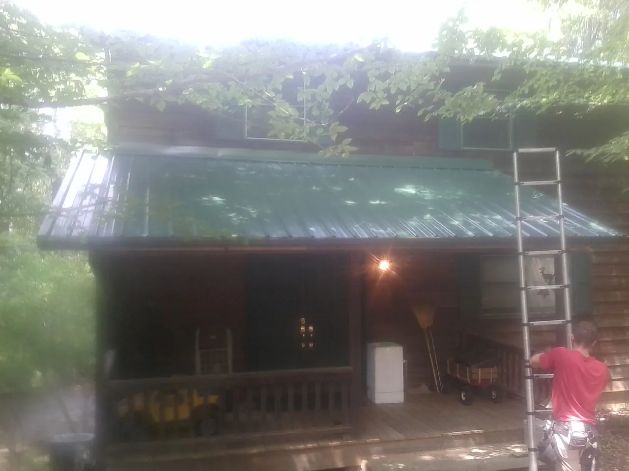 Worker on a ladder at the green porch roof of a wooded cabin in Humboldt